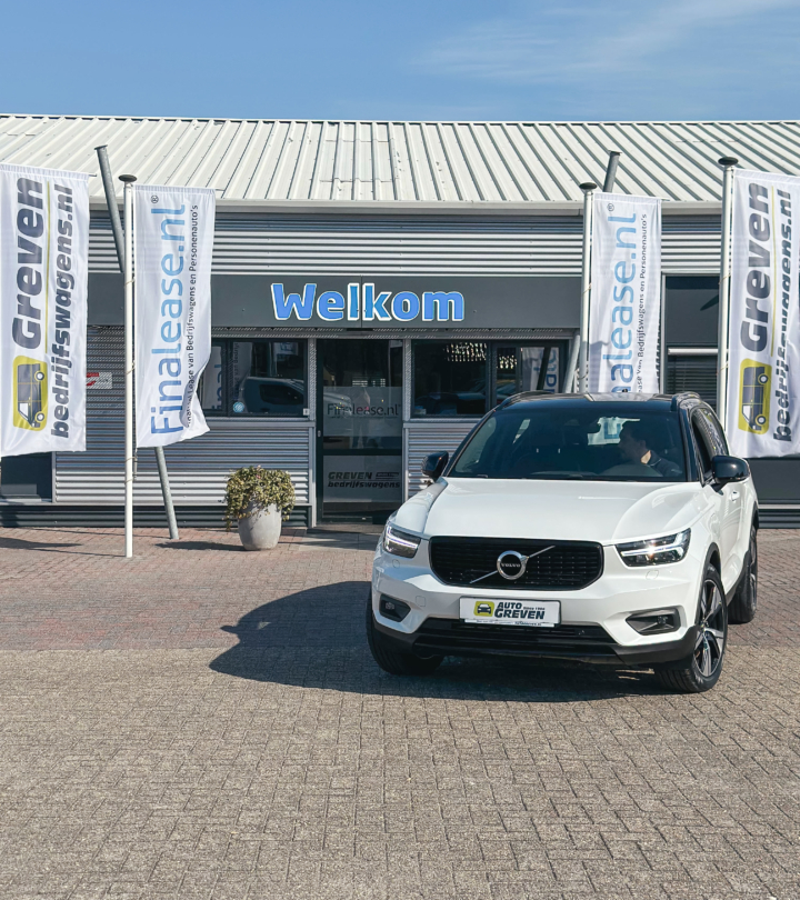 Witte Volvo SUV geparkeerd voor de ingang van Greven Bedrijfswagens, met “Welkom”-bord en banners naast het gebouw.