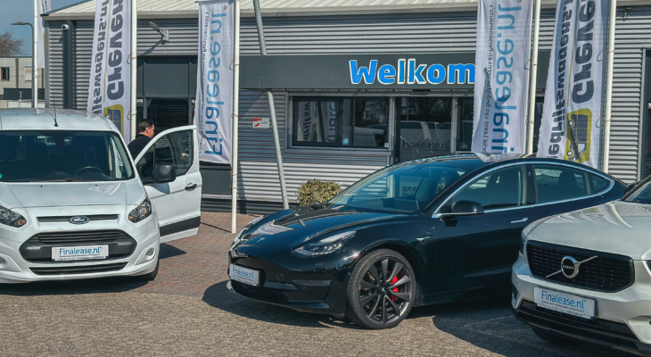Zwarte Tesla en witte Ford bedrijfswagen geparkeerd voor de ingang van Greven Bedrijfswagens, met welkom bord en banners op de achtergrond.