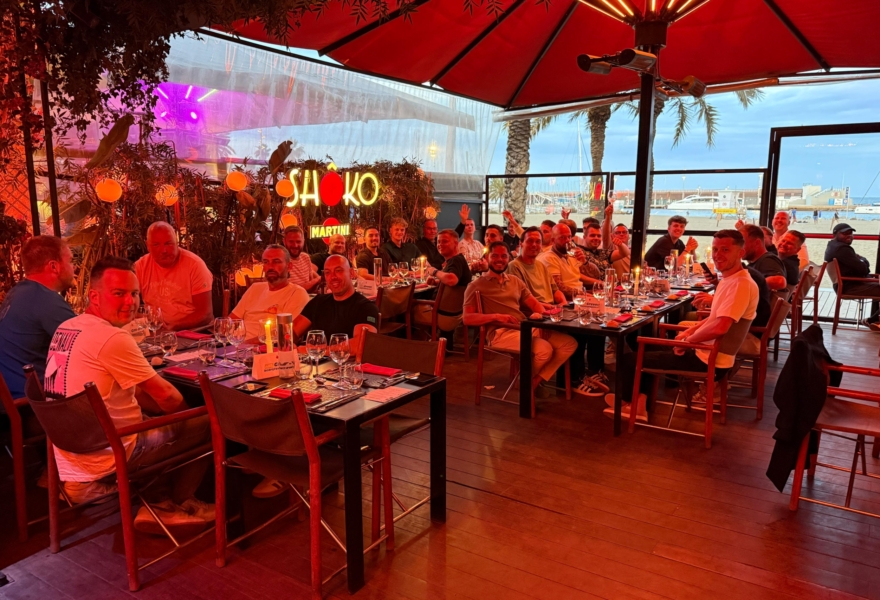 Collega’s dineren samen op een sfeervol verlicht terrasrestaurant met uitzicht op de haven in Barcelona.