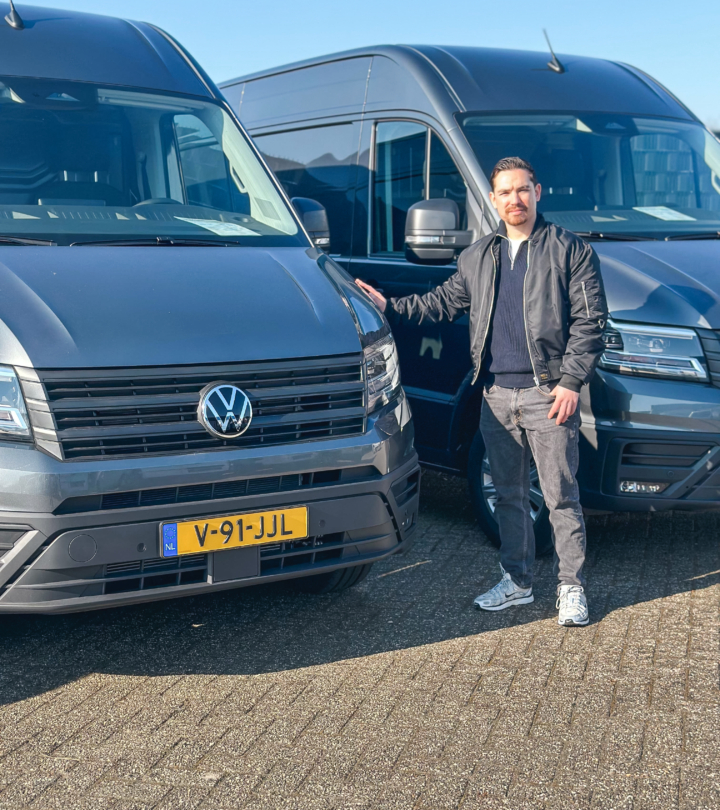 Persoon die naast een Volkswagen bedrijfswagen staat op het terrein van Greven Automotive, met meerdere Volkswagen bussen op de achtergrond.