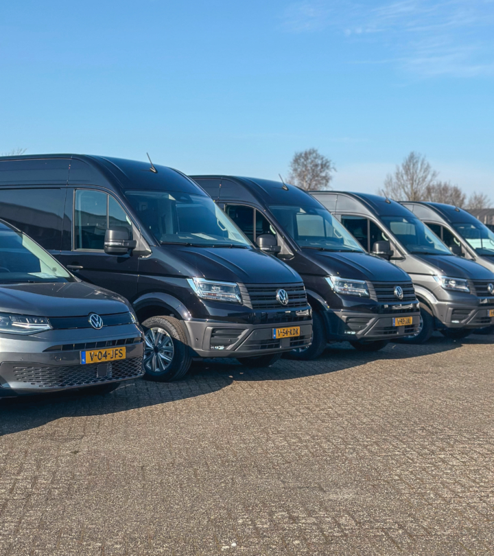 Rij zwarte en grijze Volkswagen bedrijfswagens op een buitenterrein, gefotografeerd op een zonnige dag.